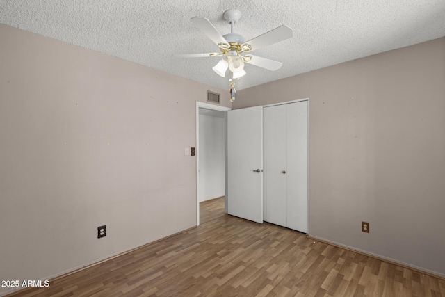 unfurnished bedroom with a textured ceiling, ceiling fan, visible vents, light wood-style floors, and a closet