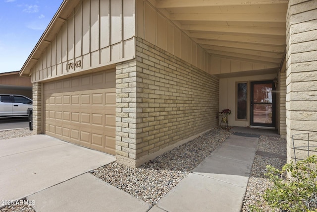 entrance to property with driveway, brick siding, board and batten siding, and an attached garage