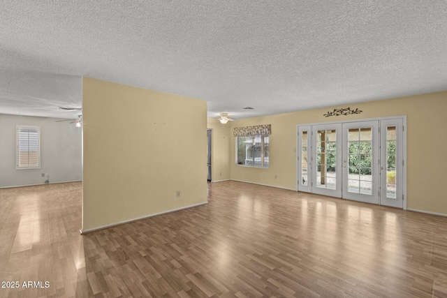 unfurnished living room with ceiling fan, a textured ceiling, baseboards, and wood finished floors