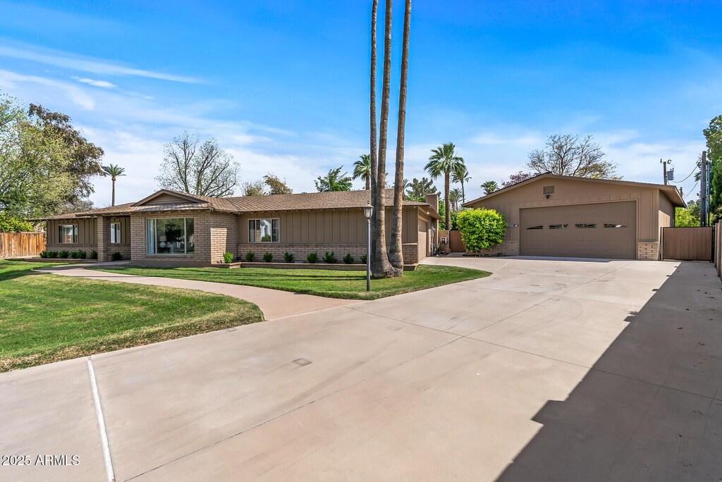 view of front facade featuring driveway, brick siding, fence, and a front yard