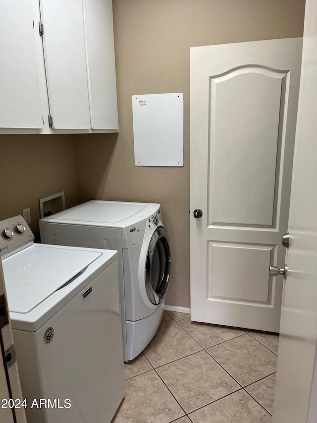 laundry area featuring washing machine and dryer, light tile patterned floors, and cabinets