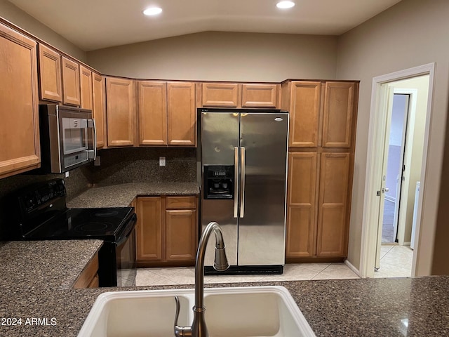 kitchen featuring sink, stainless steel appliances, dark stone countertops, vaulted ceiling, and light tile patterned floors