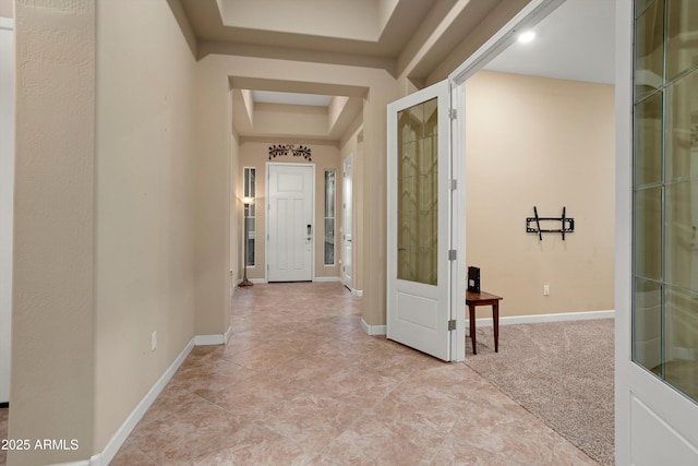 hallway featuring baseboards, a raised ceiling, and light carpet