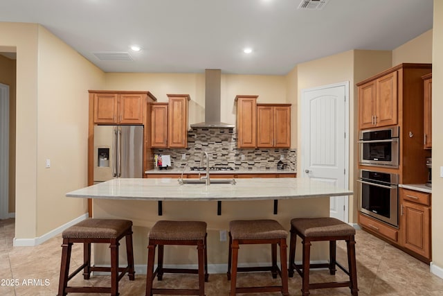 kitchen with a kitchen bar, decorative backsplash, stainless steel appliances, and wall chimney exhaust hood