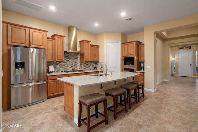 kitchen with visible vents, a sink, tasteful backsplash, stainless steel appliances, and wall chimney range hood