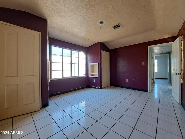 interior space with a textured ceiling, lofted ceiling, and light tile patterned flooring