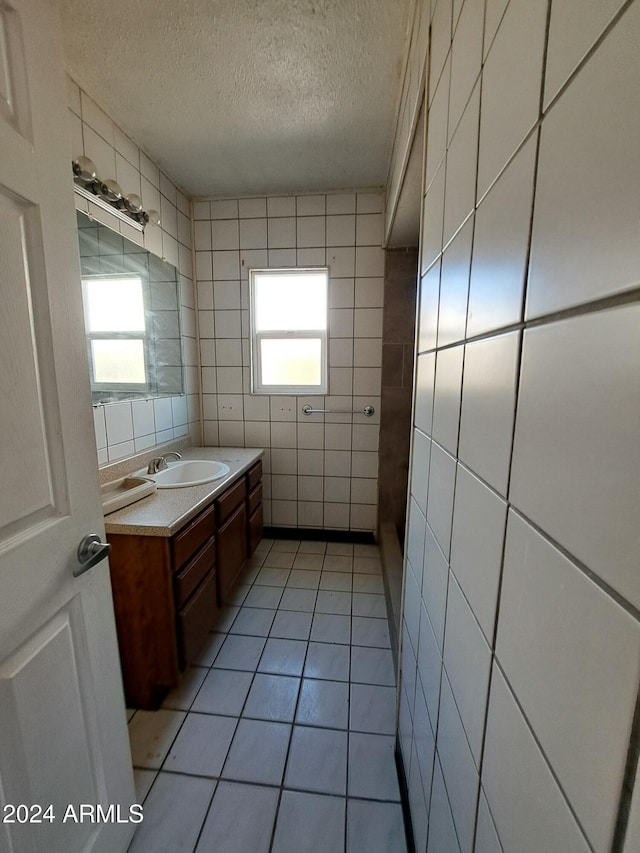 bathroom featuring a textured ceiling, tile patterned floors, vanity, and tile walls