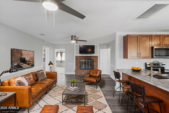 living room with a brick fireplace, hardwood / wood-style floors, and ceiling fan