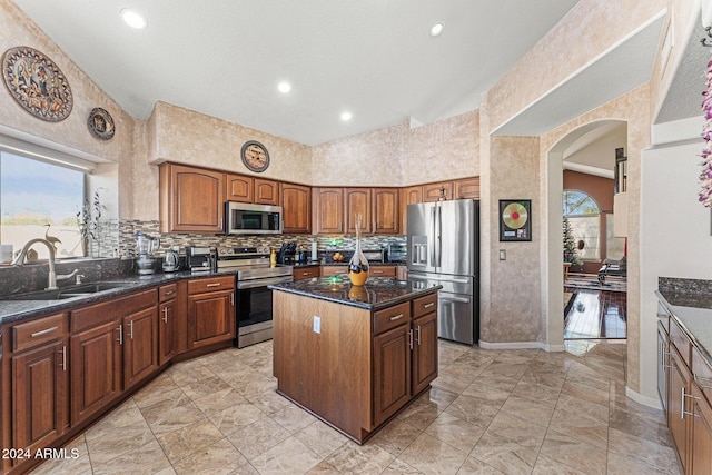 kitchen featuring stainless steel appliances, a healthy amount of sunlight, sink, dark stone countertops, and a center island