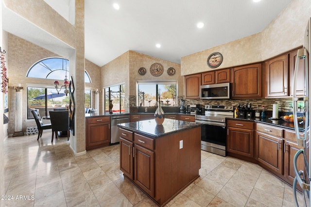 kitchen with appliances with stainless steel finishes, backsplash, dark stone counters, high vaulted ceiling, and a kitchen island