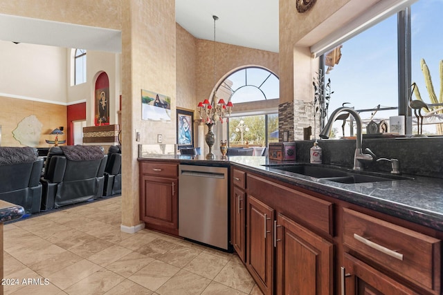 kitchen featuring sink, a high ceiling, stainless steel dishwasher, dark stone countertops, and light tile patterned floors