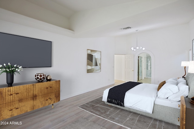 bedroom featuring visible vents, baseboards, wood finished floors, arched walkways, and high vaulted ceiling