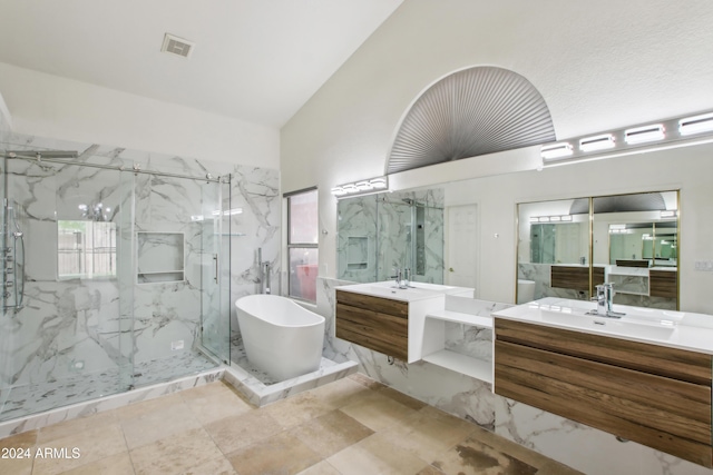 bathroom with a marble finish shower, visible vents, vaulted ceiling, two vanities, and a freestanding tub