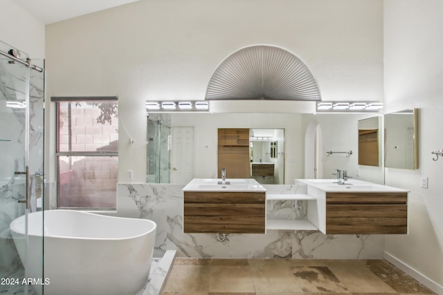 bathroom with a freestanding tub, a marble finish shower, two vanities, and a sink