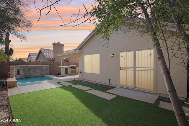 back of property at dusk with stucco siding, area for grilling, a fenced backyard, a yard, and a patio area