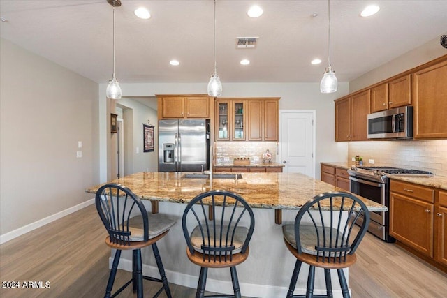 kitchen featuring light wood-type flooring, a kitchen island with sink, a breakfast bar area, hanging light fixtures, and appliances with stainless steel finishes