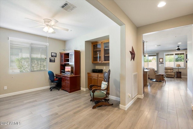 office featuring ceiling fan, light wood finished floors, built in study area, and visible vents