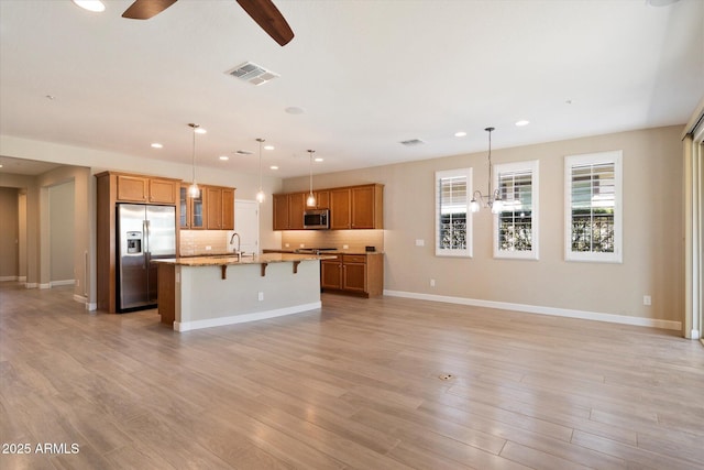 kitchen with light wood finished floors, visible vents, appliances with stainless steel finishes, a kitchen bar, and ceiling fan with notable chandelier