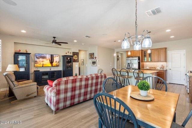 dining area with ceiling fan with notable chandelier and light hardwood / wood-style flooring