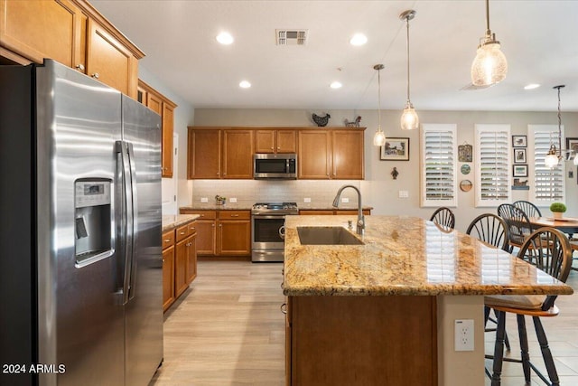 kitchen with visible vents, brown cabinetry, stainless steel appliances, a kitchen bar, and a sink