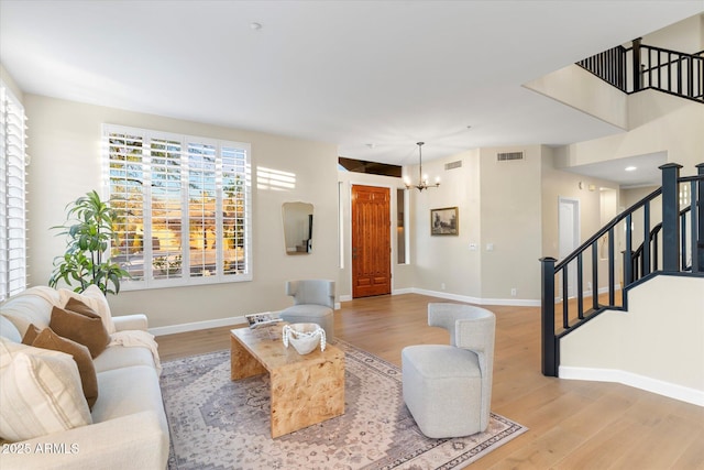 living room with a notable chandelier, light wood finished floors, visible vents, baseboards, and stairs