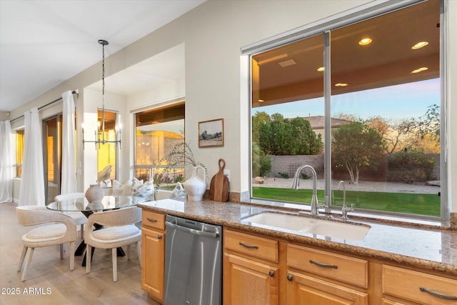 kitchen with light stone counters, wood finished floors, a sink, dishwasher, and an inviting chandelier