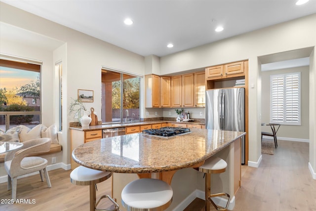 kitchen with light wood-style flooring, light stone counters, stainless steel appliances, and a kitchen breakfast bar