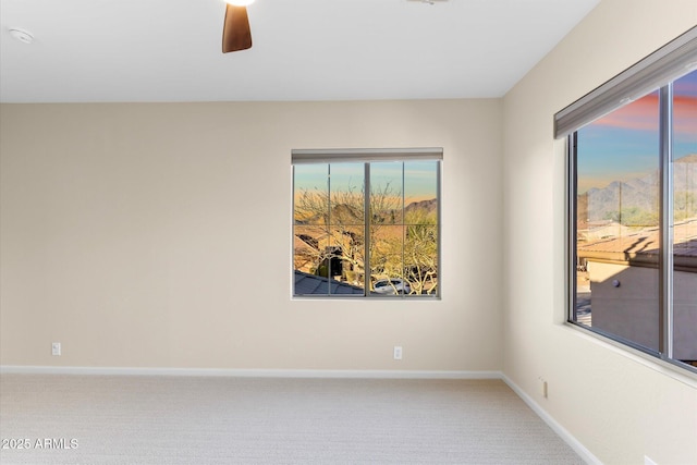 carpeted spare room featuring a ceiling fan, a wealth of natural light, and baseboards