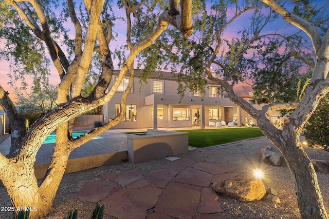 back of property featuring a patio, a lawn, and stucco siding