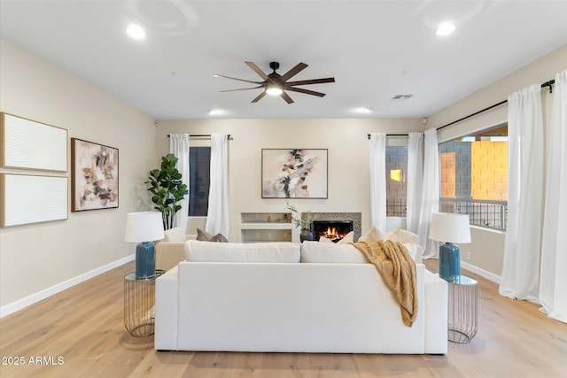 living room with a warm lit fireplace, light wood-style flooring, visible vents, and baseboards