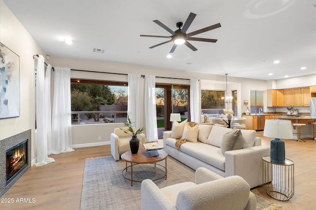 living area with light wood finished floors, baseboards, visible vents, a tiled fireplace, and recessed lighting