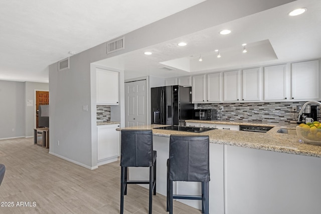 4918 N 74th St, Scottsdale, AZ 85251 - kitchen with black appliances, tasteful backsplash, a peninsula, white cabinets, and light stone countertops