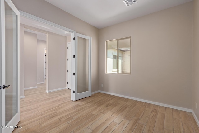 empty room featuring light wood-type flooring, baseboards, visible vents, and french doors