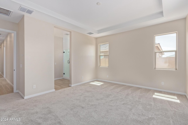 unfurnished room with a tray ceiling, carpet flooring, and visible vents