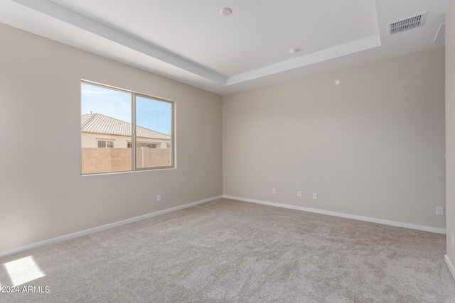 carpeted empty room featuring a raised ceiling, visible vents, and baseboards
