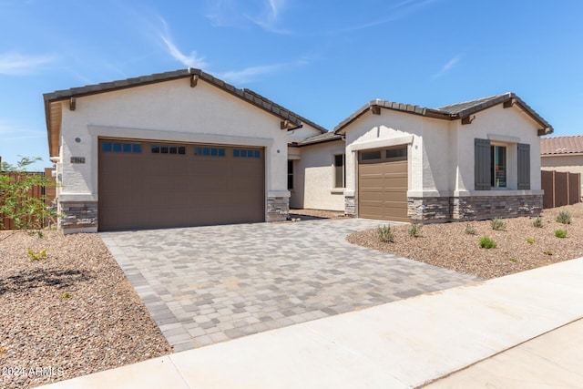 view of front of property with stone siding, decorative driveway, an attached garage, and stucco siding