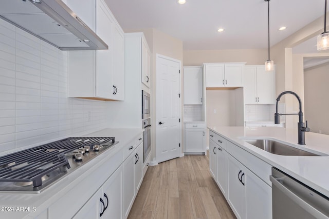 kitchen with stainless steel appliances, light countertops, white cabinets, a sink, and ventilation hood