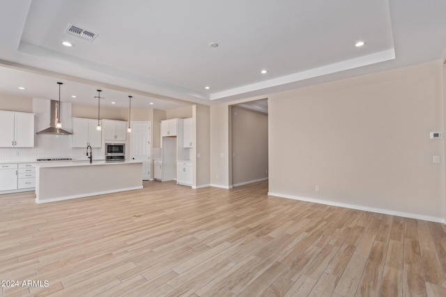 unfurnished living room with light wood-style flooring, a raised ceiling, and a sink
