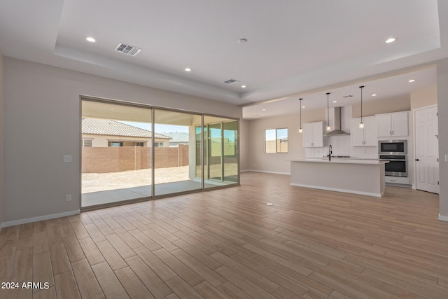unfurnished living room with light wood-style floors, visible vents, and a sink