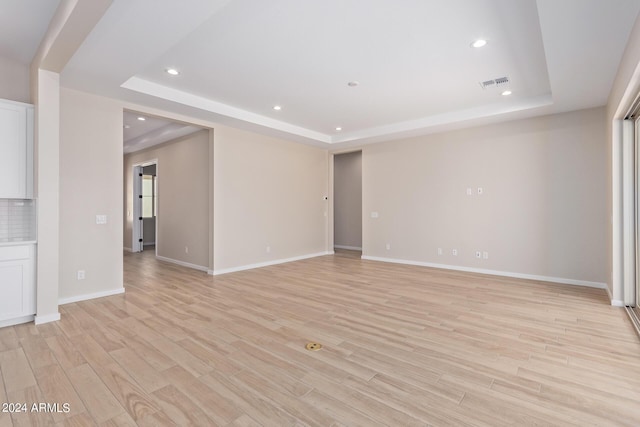 spare room with light wood-style flooring, a raised ceiling, and visible vents