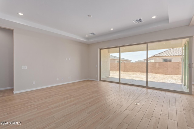 spare room with light wood-type flooring, baseboards, a tray ceiling, and recessed lighting