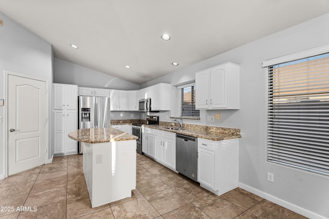 kitchen featuring lofted ceiling, a kitchen island, stainless steel appliances, white cabinets, and light stone counters