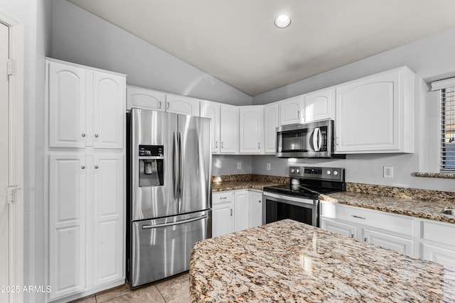 kitchen featuring appliances with stainless steel finishes, lofted ceiling, white cabinetry, light tile patterned flooring, and stone counters