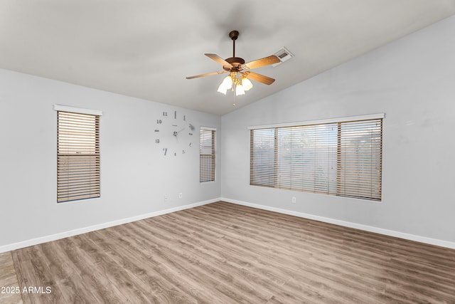 empty room featuring lofted ceiling, ceiling fan, a wealth of natural light, and hardwood / wood-style flooring