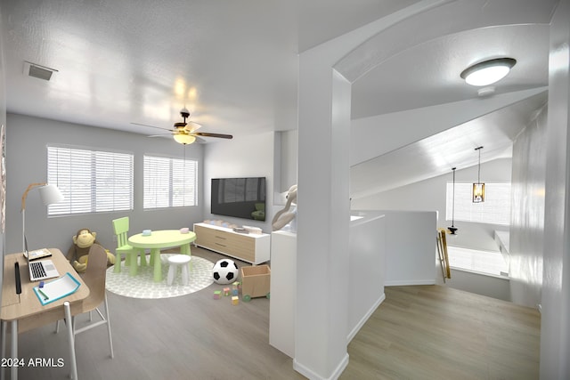 living room with lofted ceiling, a textured ceiling, ceiling fan, and light wood-type flooring