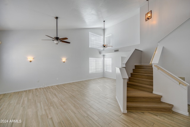 staircase featuring light wood-type flooring, ceiling fan, and a towering ceiling