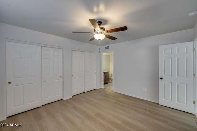 unfurnished bedroom featuring ceiling fan, ensuite bath, light hardwood / wood-style flooring, and multiple closets