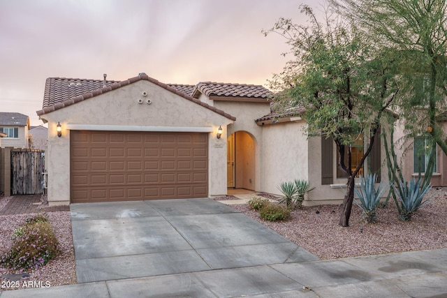 mediterranean / spanish-style home with stucco siding, a garage, concrete driveway, and a tiled roof