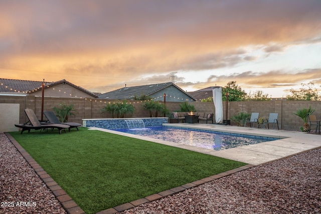 pool at dusk with a yard, a patio area, a fenced in pool, and a fenced backyard