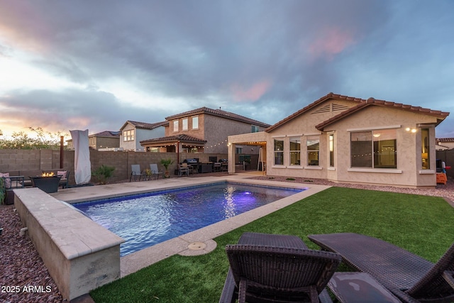 pool at dusk featuring a patio, a fenced in pool, a yard, a fenced backyard, and a fire pit